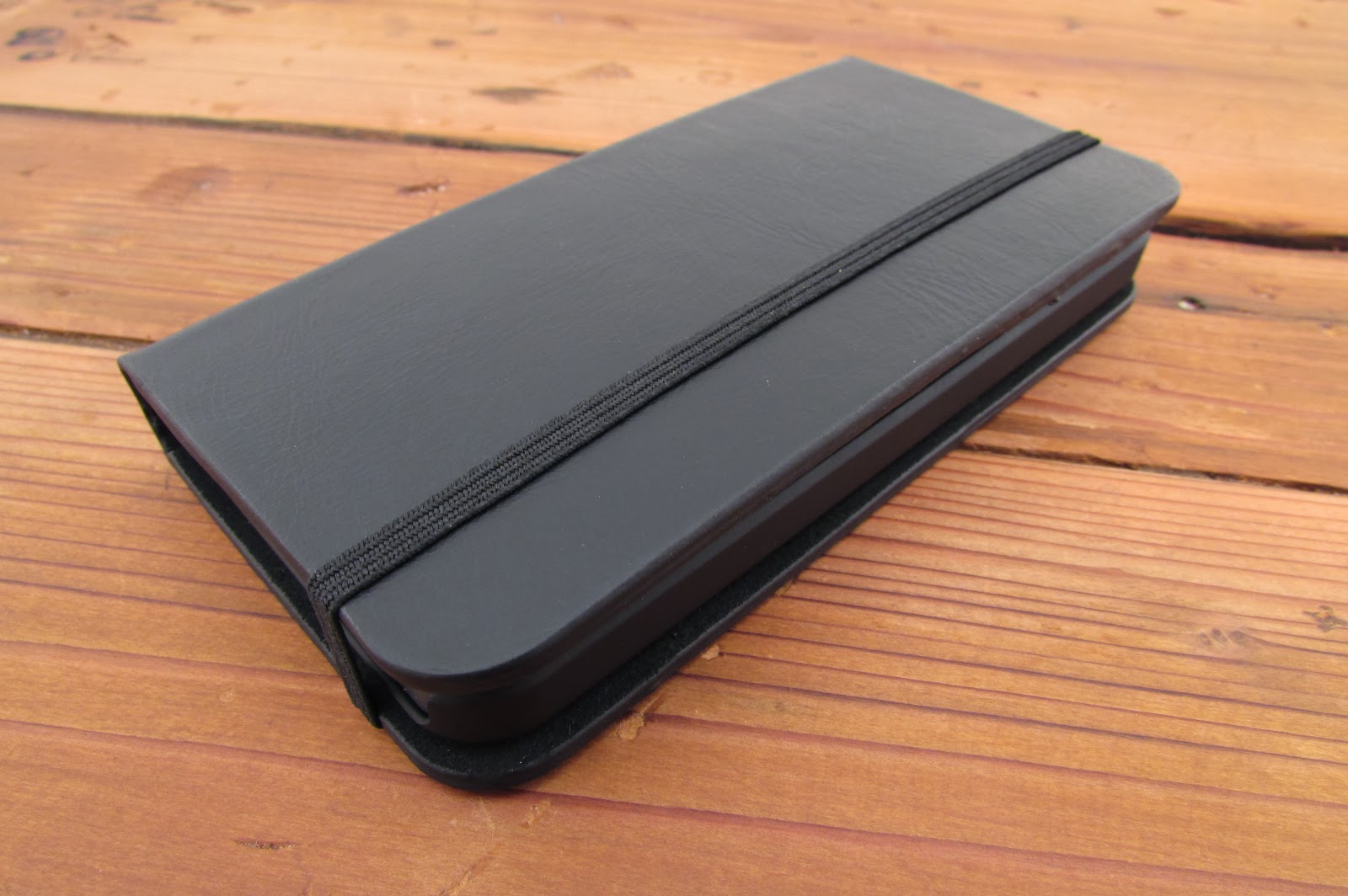 Closed black leather phone wallet case with an elastic strap, resting on a wooden table.