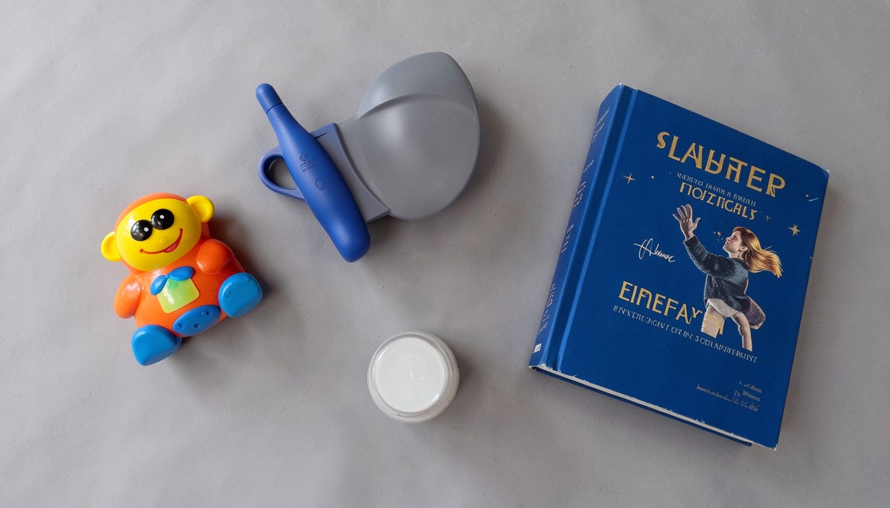Overhead flat-lay photograph of colorful product-review items — a toy, a kitchen gadget, a book, and a beauty jar — arranged on a soft gray surface with warm natural light